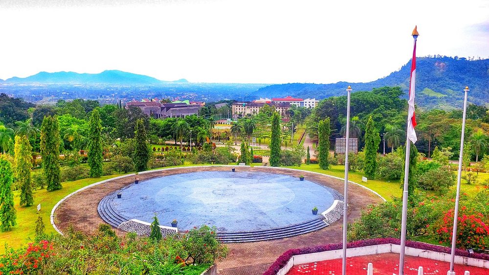 A university campus with a round pool, lawns and hills behind